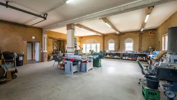 Weitläufiger Werkstattbereich mit Arbeitsplätzen, hohen Decken und Fenstern, die viel Tageslicht hereinlassen.