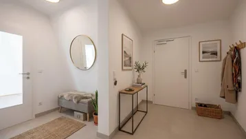 Heller Eingangsbereich mit modernen Möbeln, Spiegel und Garderobe, der einladend wirkt und gut gepflegt ist.