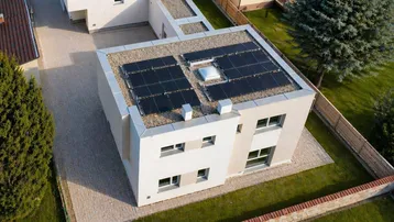 Modernes Einfamilienhaus mit Flachdach und Photovoltaikanlage, umgeben von Grünflächen.