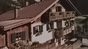 Traditionelles Alpenhaus mit mehreren Holzbalkonen und Bergblick, umgeben von grüner Natur.