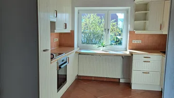 Helle Küche mit terracottafarbenen Fliesenboden, Holzdecke und Einbauschränken mit Blick ins Grüne.