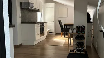 Helle offene Küche mit weißen Schränken, Laminatboden und Essbereich unter Dachschräge.