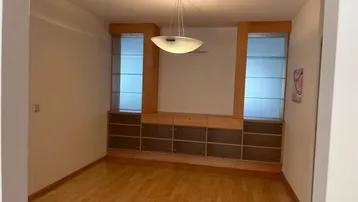 Geräumiges Wohnzimmer mit hellem Parkettboden und integrierten Holzschränken mit Glasvitrinen.