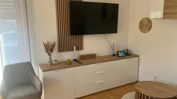 Modernes Wohnzimmer mit TV-Möbel, Holzpaneel und hellem Parkettboden, gut beleuchtet.