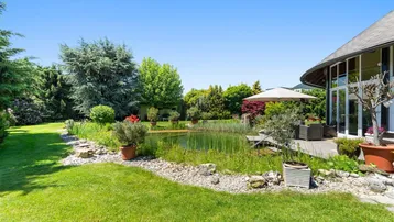 Großer Garten mit Teich, Sitzbereich und Blick auf die moderne Architektur des Hauses.