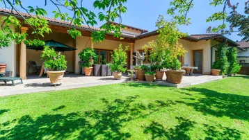 Großer gepflegter Garten mit weitläufiger Rasenfläche und sonniger Terrasse, umgeben von üppigem Grün.