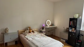 Helles Schlafzimmer mit Holzbett, Schreibtisch und einem runden Teppich auf Parkettboden.