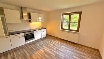 Helle Küche mit Laminatboden, weißen Schränken, integriertem Backofen und einem Fenster mit Blick ins Grüne.