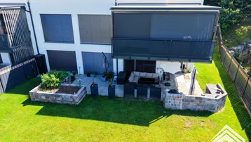 Moderne Wohnanlage mit gepflegtem Rasen, Steinterrasse und erhöhtem Blumenbeet.