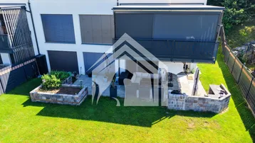 Moderne Wohnanlage mit großem Rasenbereich, möblierter Terrasse und erhöhten Gartenbeeten.