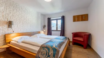 Helles Schlafzimmer mit Doppelbett, rotem Sessel und Fenster mit Bergblick.