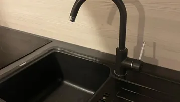 Moderne schwarze Spüle mit passendem Wasserhahn und Induktionskochfeld in der Küche.