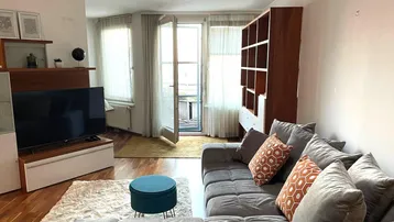 Helles Wohnzimmer mit gemütlichem Sofa, TV-Möbel und Zugang zu einem Balkon.