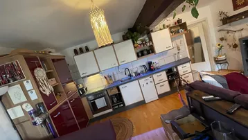 Funktionale Küche mit weißen Schränken, integrierten Geräten und Holzbalken in einem offenen Wohnkonzept.
