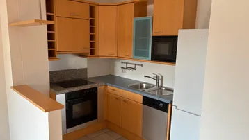 Kleine Einbauküche mit Holzschränken, Elektrogeräten und Granitarbeitsplatte.