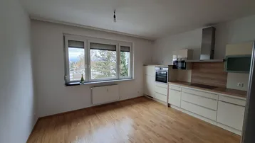 Helle Küche mit Holzboden, Einbaugeräten und Blick ins Grüne durch das große Fenster.