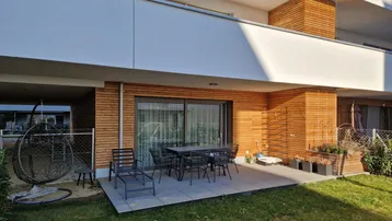 Moderne Terrasse mit Gartenmöbeln und Zugang zum privaten Gartenbereich eines Neubaus.