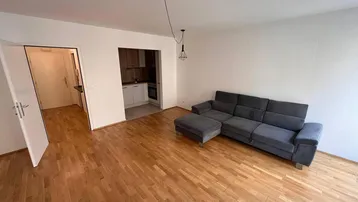 Heller Wohnbereich mit Parkettboden und integrierter Küchenzeile, ideal für offenes Wohnen.