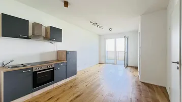 Heller offener Wohnbereich mit integrierter Küchenzeile, Parkettboden und Zugang zum Balkon.