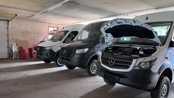 Geräumige Garage mit mehreren Fahrzeugen und geöffneter Motorhaube für Wartungsarbeiten.