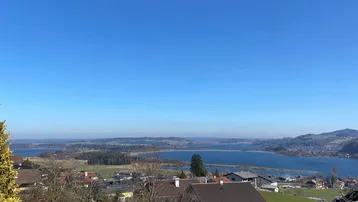 Weitläufiger Blick über einen See und die umliegende Landschaft mit vereinzelten Häusern.