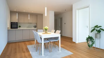 Moderne offene Küche mit Essbereich, Holzboden und hellen Schränken in einem lichtdurchfluteten Raum.
