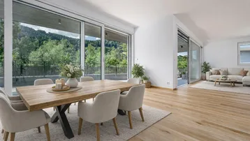 Heller, offener Wohn- und Essbereich mit Holztisch, bequemen Stühlen und Zugang zur Terrasse mit Bergblick.