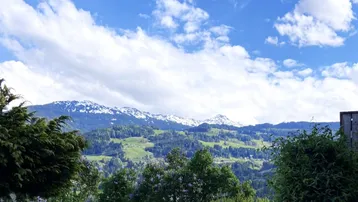 Panoramablick auf schneebedeckte Berge und grüne Hügel unter blauem Himmel.