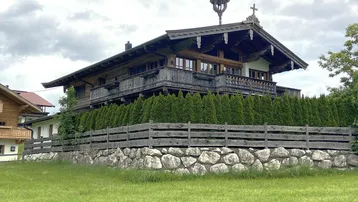 Traditionelles Holzhaus im Chalet-Stil mit Balkonen und Steinfundament, umgeben von Hecken und Wiesen.