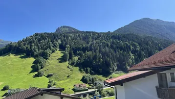 Malerischer Blick auf grüne Berge und bewaldete Hänge mit Häusern im Tal.