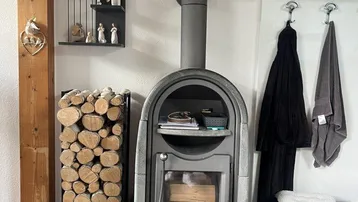 Moderner Holzofen mit gestapeltem Brennholz und Garderobe in einem Innenraum.