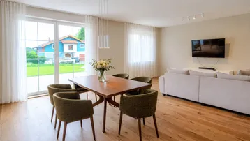 Heller Essbereich mit Holztisch, grünen Stühlen und Zugang zum Garten durch große Schiebetüren.