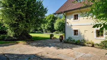 Gedeckte Terrasse mit Natursteinplatten und Blick auf den weitläufigen Garten und die umliegende Natur.