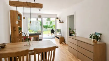 Heller Wohn- und Essbereich mit Holzboden, rustikalem Esstisch und Zugang zum Garten.