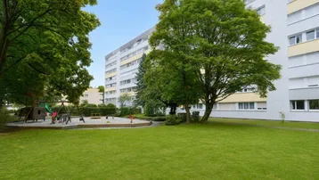 Große Grünfläche mit Spielplatz und Bäumen vor einem Mehrfamilienhaus.