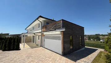 Modernes Einfamilienhaus mit Holzfassade, gepflasterter Auffahrt und integrierter Garage.