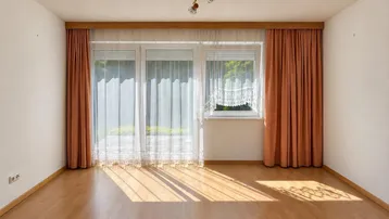 Helles Wohnzimmer mit Parkettboden und Zugang zu einem kleinen Außenbereich, gut beleuchtet durch große Fenster.