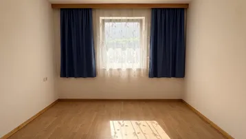 Helles, leeres Zimmer mit Laminatboden und Fenster, das viel Tageslicht hereinlässt.