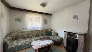 Gemütliches Wohnzimmer mit großem Sofa, Holzboden und einem traditionellen Kaminofen.