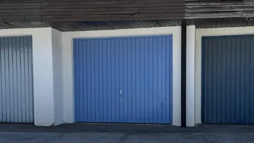 Nahaufnahme einer blauen Garagentür mit weißem Rahmen und Holzelementen darüber.