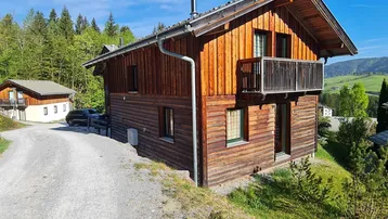 Rustikales Holzhaus im alpinen Stil mit Balkon und umgeben von grüner Natur.