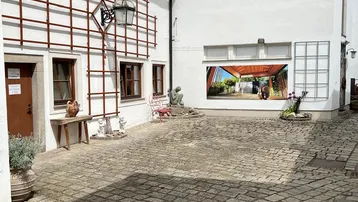 Gepflasterter Innenhof mit weißen Gebäudefassaden, dekorativen Rankgittern und einem großen Wandbild.