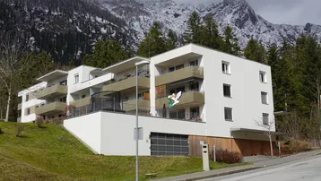 Modernes Mehrfamilienhaus mit Balkonen und Bergblick in alpiner Umgebung.