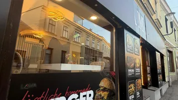 Außenansicht eines Geschäftsgebäudes mit großen Schaufenstern und Werbung für Burger und andere Speisen.