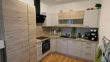 Moderne Einbauküche mit hellen Holz- und Grautönen, Laminatboden und integrierten Kochgeräten.