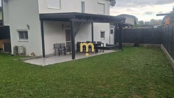 Modernes Haus mit überdachter Terrasse, Gartenmöbeln und großem Rasenbereich.