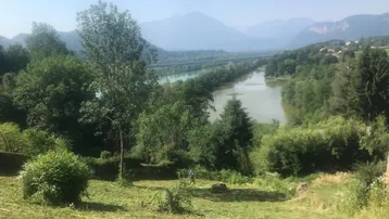 Weitläufiger Blick über eine grüne Landschaft mit Fluss, Bergen und klarem Himmel an einem sonnigen Tag.
