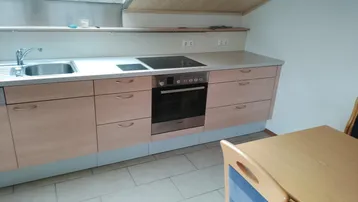 Kleine Küche mit hellen Holzschränken, Induktionskochfeld und Dachschräge, gut beleuchtet durch ein Dachfenster.