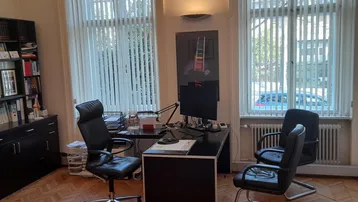 Helles Büro mit Fischgrätparkett, zwei großen Fenstern und modernem Arbeitsplatz.