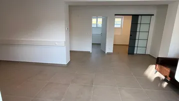 Geräumiger, heller Büroraum mit modernen Fliesenböden und Schiebetür zu einem weiteren Bereich.